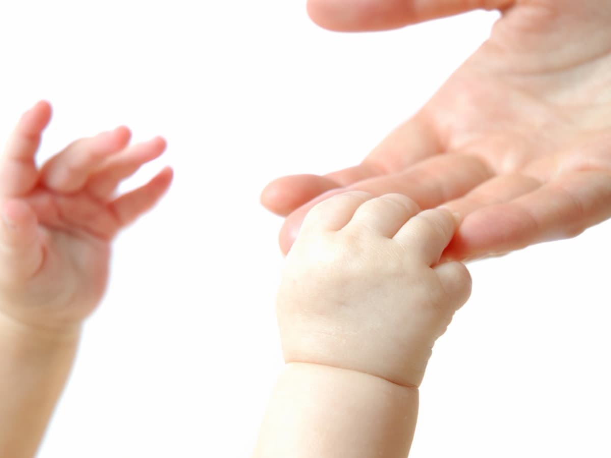 Die Hand eines Babys und die Hände einer erwachsenen Person berühren sich